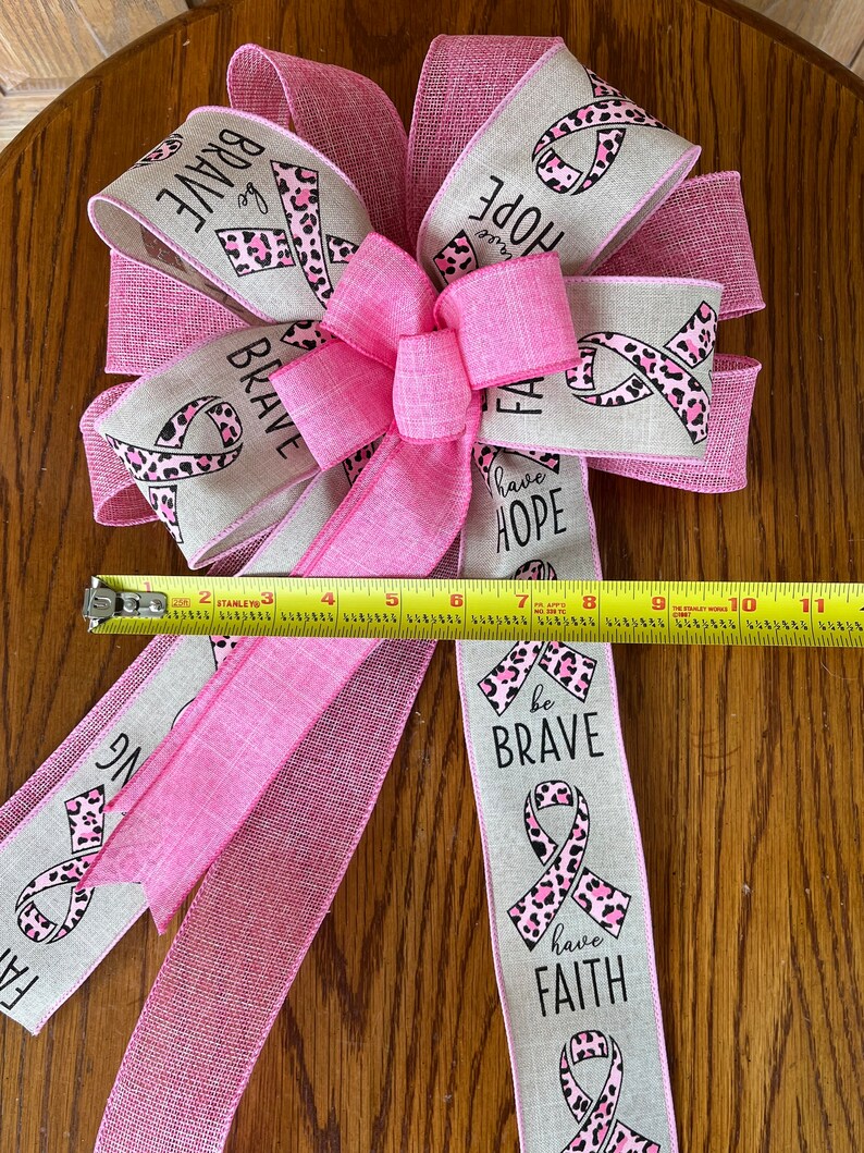 May include: A pink and beige ribbon bow with a leopard print and the words "be brave", "have hope", and "have faith".