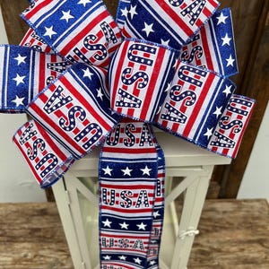 May include: A red, white, and blue ribbon bow with the word "USA" printed on it. The bow is tied around a white lantern.
