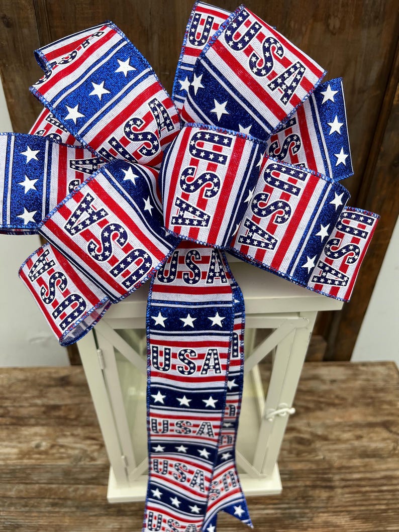 May include: A red, white, and blue ribbon bow with the word "USA" printed on it. The bow is tied around a white lantern.