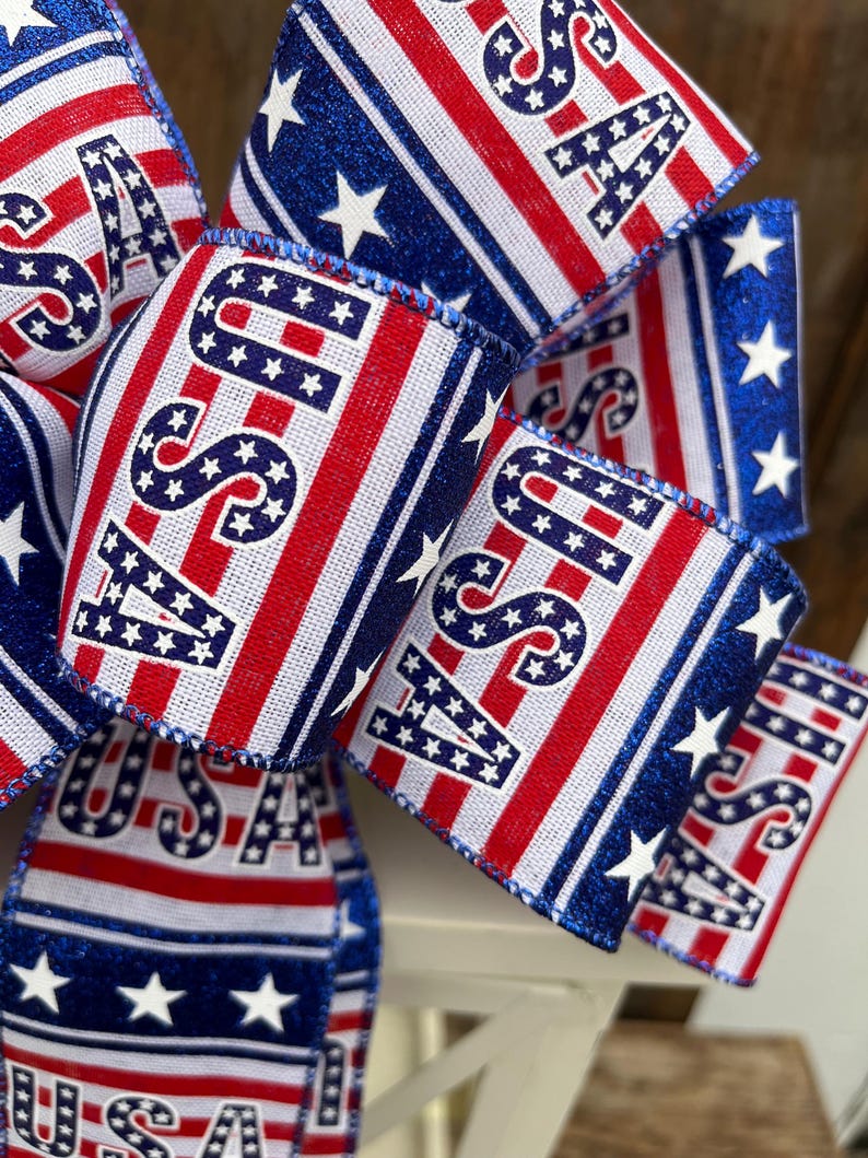 May include: A red, white, and blue ribbon bow with the word "USA" printed on it. The ribbon has a glittery blue stripe and white stars.
