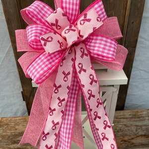 May include: A pink and white gingham ribbon bow with pink ribbon tails featuring a pink glitter ribbon with pink ribbon designs. The bow is tied around a white lantern.