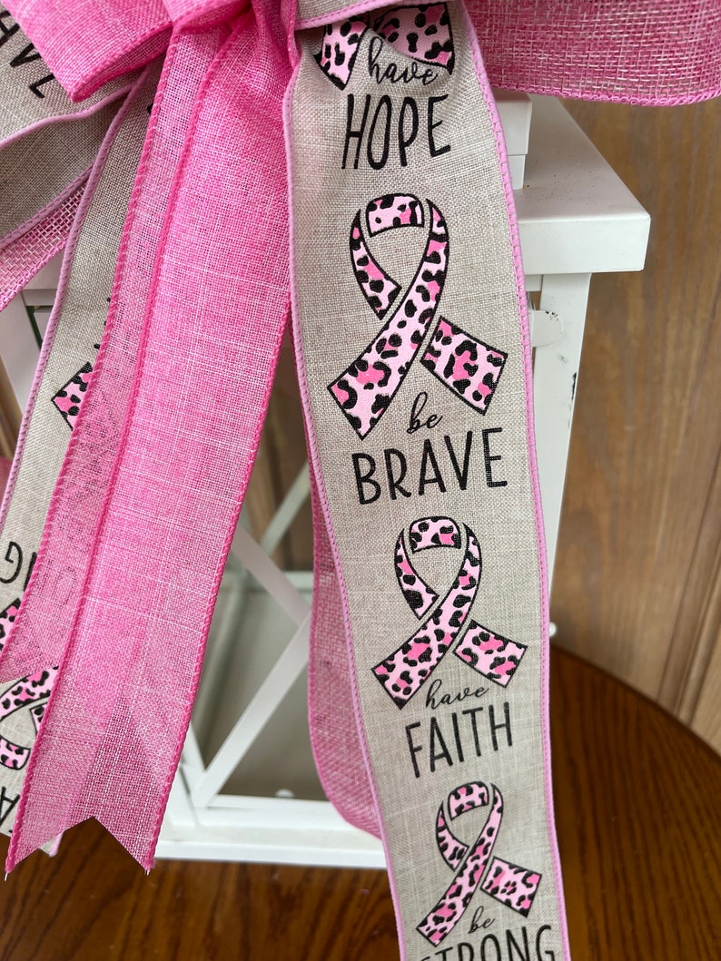 May include: A pink and beige ribbon with a pink leopard print ribbon and the words "have hope", "be brave", "have faith", and "be strong" printed on it.