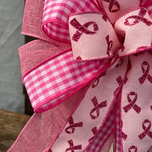 May include: Pink and white gingham ribbon, pink ribbon with pink glitter, and pink mesh ribbon tied into a bow. The ribbon is decorated with pink glitter ribbons.