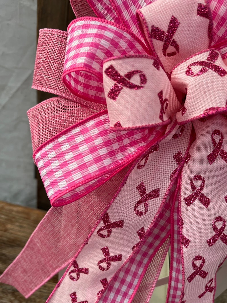 May include: Pink and white gingham ribbon, pink ribbon with pink glitter, and pink mesh ribbon tied into a bow. The ribbon is decorated with pink glitter ribbons.