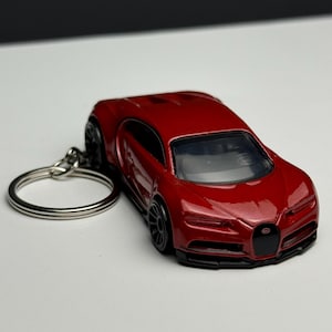 May include: A red die-cast model car keychain. The miniature car features a sleek design with black wheels and a black front grille. The keychain ring is silver.