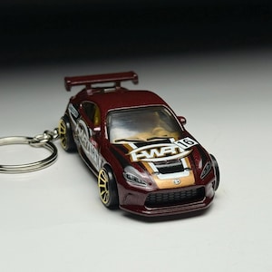 May include: A burgundy toy car keychain with gold-colored wheels and accents. The car has a spoiler and the text "FWR 16" on the hood. The keychain ring is silver.