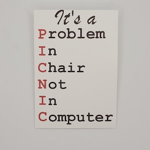 May include: White card with black text that reads "It's a Problem In Chair Not In Computer". The letters "P.I.C.N.I.C" are in red.