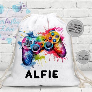 May include: White drawstring bag with a vibrant watercolour design of a games controller. The controller is in shades of blue, yellow, orange, and purple with the name "ALFIE" in black. Matching lunch bag and towel available.