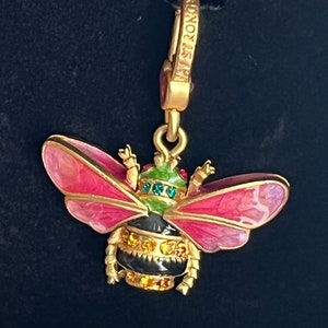 Op de afbeelding: Een gouden bedel in de vorm van een bij met roze en groene emaille vleugels en een zwart en gouden lichaam met heldere strass steentjes. De bedel is bevestigd aan een gouden ketting met een sluiting waarop "THOMAS SABO" staat.