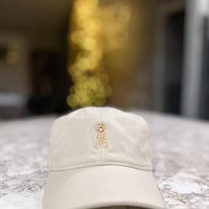 Puede incluir: Una gorra de béisbol beige con una imagen bordada de un golden retriever.