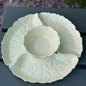 May include: A pale yellow ceramic serving set consisting of a central round bowl surrounded by three leaf-shaped dishes. Each piece features a raised leaf vein texture and a speckled finish, creating a cohesive botanical design for food service.