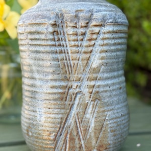 May include: A handmade ceramic vase with a textured, ribbed surface and a light blue and brown color scheme. The vase features an etched design of intersecting lines. The vase is a decorative item for the home.