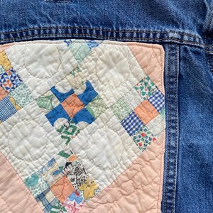 May include: Close-up of a denim jacket with a quilted patch. The patch features a patchwork design with squares of various patterns and colors, including blue, green, orange, and floral prints. The quilt is set against a light pink background.