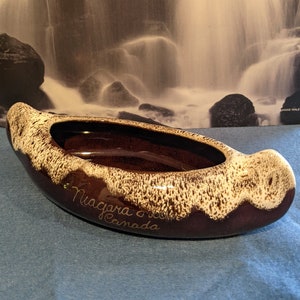 May include: A brown and white ceramic canoe-shaped dish with the words "Niagara on the Lake Canada" inscribed on the side.