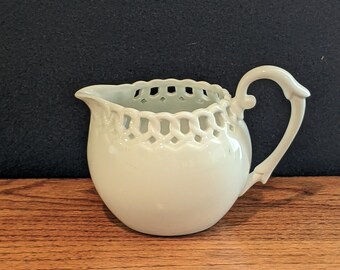 May include: White porcelain creamer with a delicate openwork design around the rim and a fluted handle.