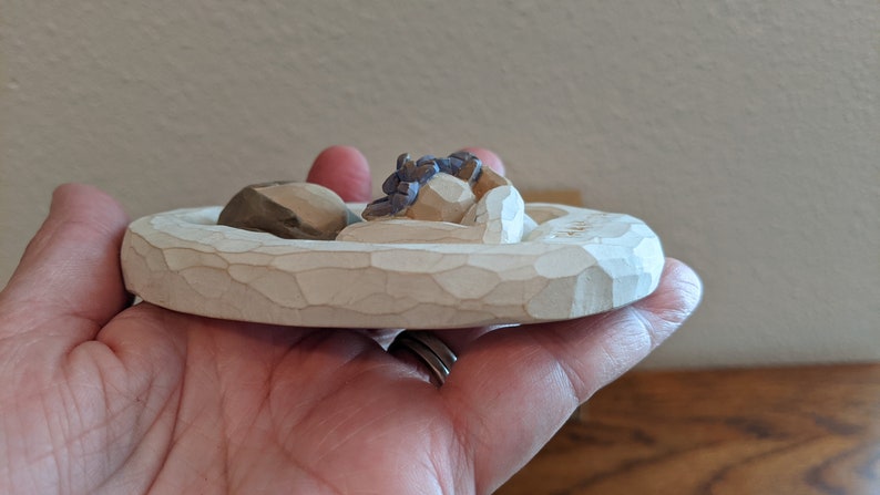 Puede incluir: Una peque&ntilde;a figura de madera blanca de una pareja durmiendo en una cama. La figura est&aacute; tallada con detalles y tiene un aspecto r&uacute;stico.
