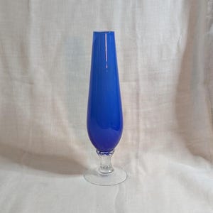 May include: A striking cobalt blue glass vase, featuring a teardrop shape and a clear, circular base. The vase has a detailed stem. The smooth, glossy finish contrasts with the textured stem. This decorative vase is suitable for displaying flowers.