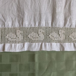 May include: White linen tea towel with a crocheted lace border. The lace has a delicate floral pattern.