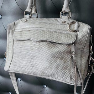 Pu&ograve; includere: Una borsa grigio chiaro con un motivo a pelle di serpente. La borsa ha due manici superiori, una tracolla e finiture argentate. &Egrave; dotata di una tasca frontale con cerniera e uno scomparto principale. La borsa &egrave; realizzata in un materiale strutturato.