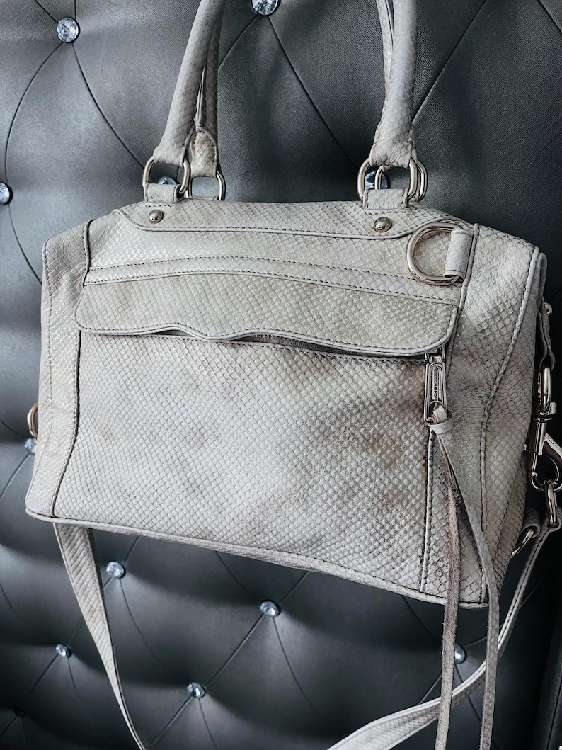 Pu&ograve; includere: Una borsa grigio chiaro con un motivo a pelle di serpente. La borsa ha due manici superiori, una tracolla e finiture argentate. &Egrave; dotata di una tasca frontale con cerniera e uno scomparto principale. La borsa &egrave; realizzata in un materiale strutturato.