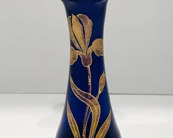 May include: A cobalt blue glass vase with a ruffled rim and a flared base. The vase is adorned with a gold iris flower design. The elegant vase is a decorative home accent.