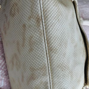 Pu&ograve; includere: Primo piano di una borsa color crema con un motivo a pelle di serpente. La borsa ha una chiusura con cerniera e finiture color oro. La borsa mostra segni di usura con scolorimento.