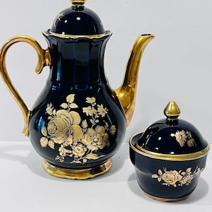 May include: A navy blue porcelain tea set with gold accents. The set includes a teapot with a lid and a sugar bowl with a lid. Both pieces are decorated with gold floral designs.