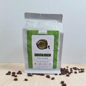 May include: A white bag of Costa Rican single-origin coffee beans. The bag features a green label with the text "COSTA RICA PEREZ ZELEDON" and "250g | Coffee Beans". Coffee beans are scattered in front of the bag.