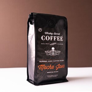Könnte beinhalten: Schwarzer Kaffeepackung mit dem Text "Whiskey Barrel COFFEE" und "Mocha Java". Die Packung zeigt eine Totenkopf-Grafik und trägt die Aufschrift "Small Batch Roasted in Colorado". Die Packung enthält ganze Kaffeebohnen.