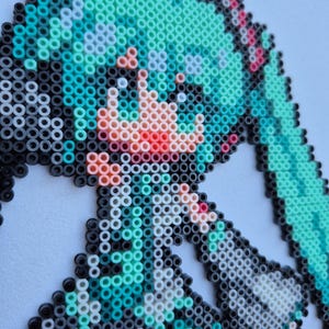 May include: Pixel art portrait of a character with turquoise hair, created with colorful plastic beads. The artwork features a detailed face with pink and red accents, set against a white background. The beads are arranged to form a recognizable anime-style image.