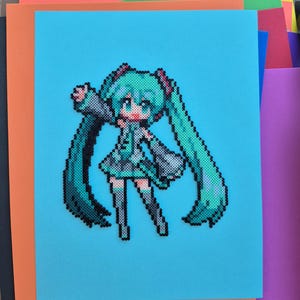 May include: A pixel art depiction of a character with long, turquoise pigtails, a matching outfit, and large eyes. The artwork is created with small, colorful beads on a light blue background, with orange and other colored paper in the background.