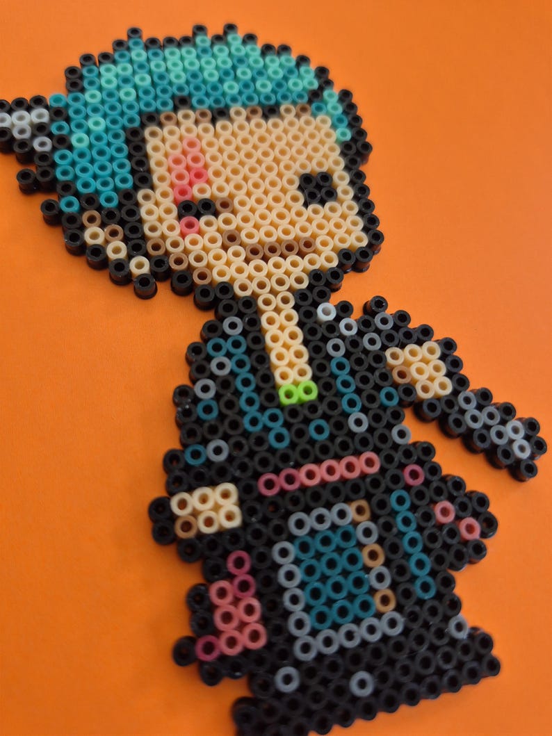 May include: A pixel art figure made from colorful plastic beads. The figure has blue hair, a black outfit, and a light skin tone. The background is a solid orange color.