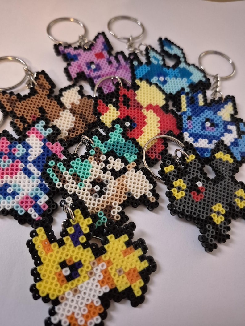 May include: A collection of colorful pixelated keychains featuring various Pokemon characters. The keychains are made of small plastic beads and are attached to silver key rings.