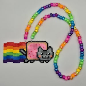 May include: A necklace featuring a pixelated cat character with a pink body and a rainbow trail, crafted from small square beads. The pendant is attached to a long chain made of colorful, translucent plastic pony beads in a repeating rainbow pattern.
