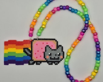 May include: A necklace featuring a pixelated cat character with a pink body and a rainbow trail, crafted from small square beads. The pendant is attached to a long chain made of colorful, translucent plastic pony beads in a repeating rainbow pattern.