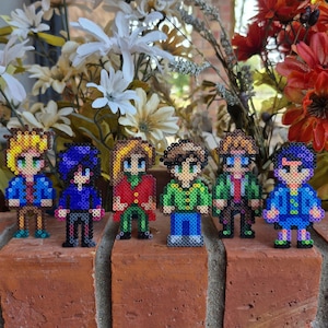 May include: Six pixel art figures made of colorful beads, standing on a brick surface. The figures are all different colors and have different hairstyles and clothing.