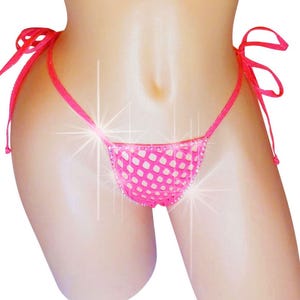 May include: A bright pink thong bikini bottom with white polka dots. The bikini has tie sides and a small, low-rise cut. The fabric has a mesh-like appearance. The bikini is displayed on a mannequin.