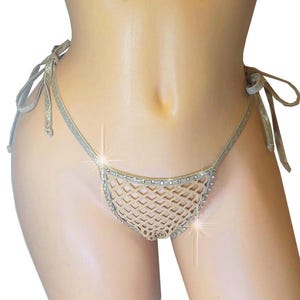 May include: A gold-colored, net-style bikini bottom with rhinestone accents. The bikini bottom features tie closures on each side. The garment is displayed on a mannequin.