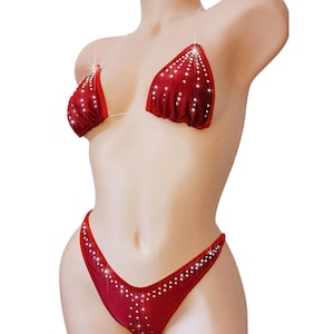 May include: A red bikini set with sparkling embellishments. The top features triangle cups with a string tie, and the bottoms are a high-cut style. The entire set is adorned with small, shimmering accents.