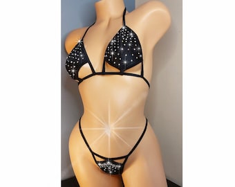 Puede incluir: Conjunto de lencería negra con un sujetador triangular y una tanga. Ambas piezas están adornadas con pedrería.