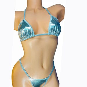 May include: A light blue metallic bikini set. The top is a triangle style with halter straps, and the bottom is a thong style. The fabric has a shiny, reflective quality. The bikini is displayed on a mannequin.