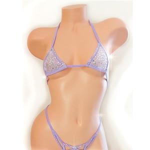 May include: A lavender bikini set with sparkling embellishments. The triangle top and the bottom are adorned with shimmering rhinestones. The bikini is displayed on a mannequin.