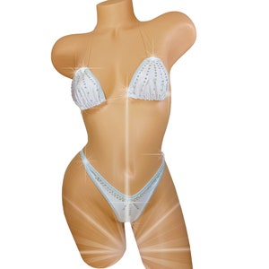 May include: A white bikini with crystal embellishments. The top is a triangle style with thin straps and the bottom is a cheeky cut.