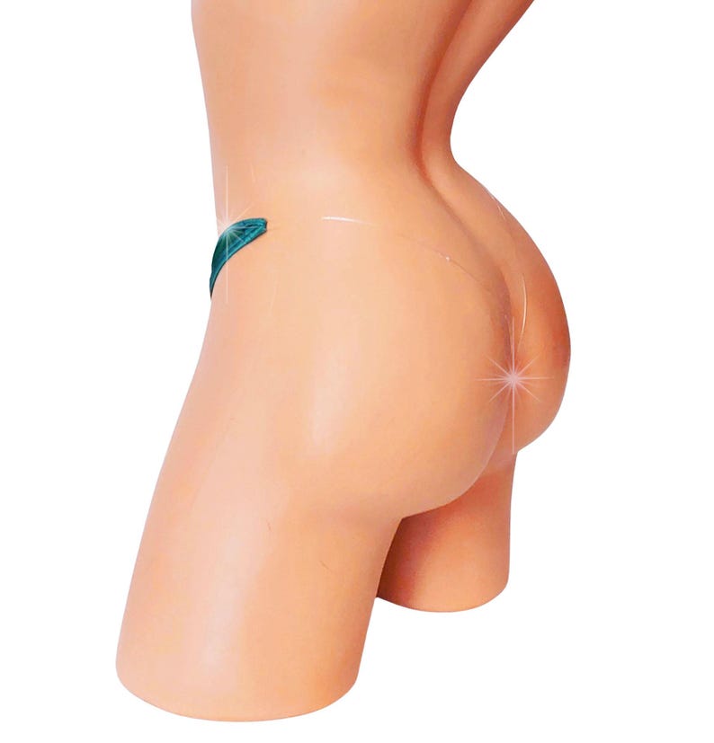 May include: A mannequin torso, viewed from the side and rear, with a light skin tone. A teal thong is visible. The mannequin is set against a white background. The image is well-lit, highlighting the form.