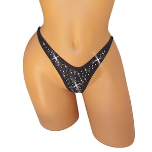 May include: Black thong-style underwear with a V-shaped front and sparkling rhinestone embellishments. The underwear is displayed on a mannequin, showcasing the design and fit. The rhinestones are arranged in a scattered pattern.