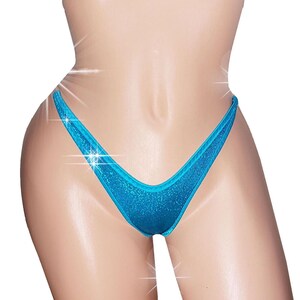 May include: A close-up of a turquoise bikini bottom with a shimmering, glittery texture. The bikini bottom has a classic thong style with a low-rise waist and a V-shaped front.
