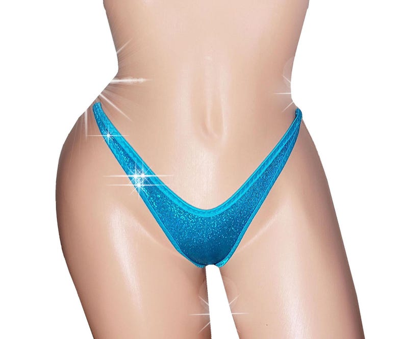 May include: A close-up of a turquoise bikini bottom with a shimmering, glittery texture. The bikini bottom has a classic thong style with a low-rise waist and a V-shaped front.