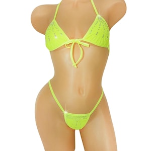 May include: Neon yellow bikini set with rhinestone embellishments. The halter top features a tie closure at the bust, and the bottoms are a thong style. The swimwear is displayed on a mannequin.