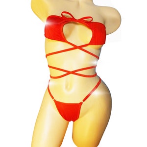 May include: Red lingerie set on a mannequin. The set includes a strapless top with a bow and a keyhole cutout, and a thong bottom. The top has straps that wrap around the torso. The lingerie is made of a soft, textured fabric.