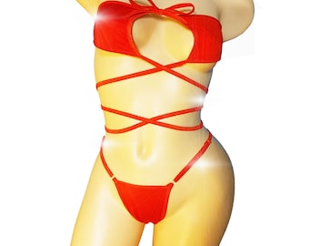 Può includere: Completo di lingerie rosso su un manichino. Il set include un top senza spalline con fiocco e scollo a cuore, e uno slip a perizoma. Il top ha delle cinghie che si avvolgono attorno al busto. La lingerie è realizzata in un tessuto morbido e strutturato.
